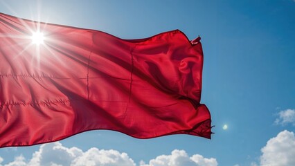 Bright red flag waving in the wind under a sunny sky with a lens flare and clouds.