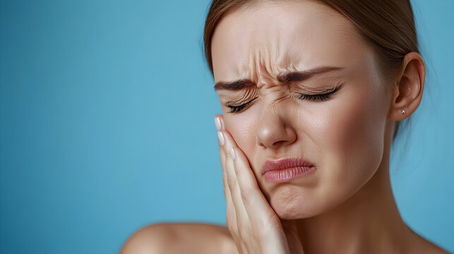 Close-up of a woman suffering from temporomandibular joint disorder, holding her jaw in pain, illustrating facial discomfort and medical concept of TMJ dysfunction or jaw joint inflammation.