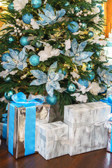 Elegantly wrapped presents, gift boxes is placed beneath decorated Christmas tree, adorned with blue and silver ornaments, creating cheerful holiday atmosphere of Christmas and New Year celebrations