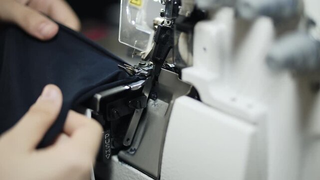 Hands sewing fabric on industrial overlock machine in textile workshop