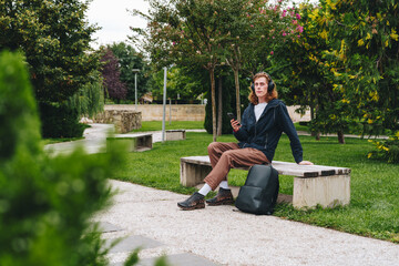 Young person relaxing on a park bench while using a smartphone in a green space