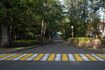yellow and white zebra crossing, flanked by lush green trees and stone walls. road stretches into the distance, surrounded by nature,