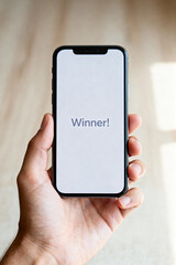 Hand holding a smartphone displaying the message "Winner!", celebratory mood, bright background

