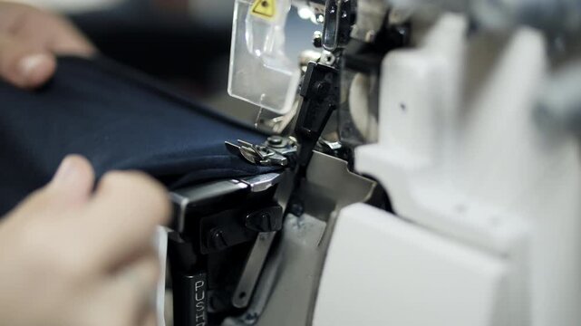 Close up of hands sewing fabric with industrial overlock machine in workshop