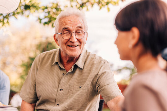 Smiling grandfather talking with granddaughter in back yard at reunion party
