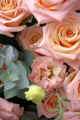 Delicate peach-colored roses and light pink lisianthus flowers with fresh water droplets, surrounded by green eucalyptus leaves.