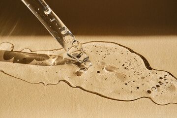 A pipette with cosmetic serum on a beige background.