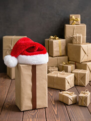 A red Santa hat rests atop a large wrapped box surrounded by many brown paper parcels on a wooden floor, evoking the warmth and anticipation of the busy holiday gift season.