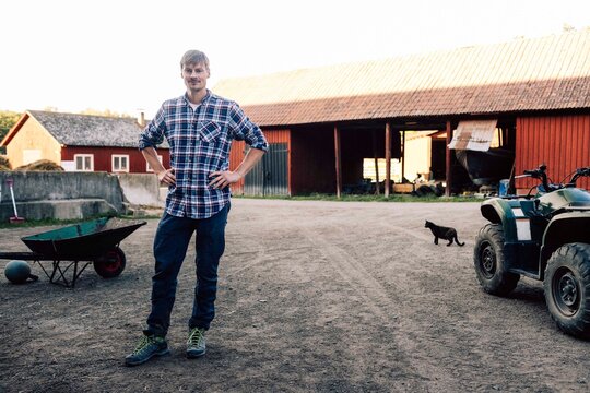 Portrait of confident farmer posing with arms akimbo in front of barn