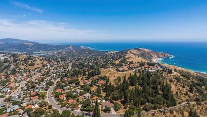 Aerial view of coastal landscape with hills, houses, and ocean, showcasing scenic beauty and terraced land near the shoreline. The image captures a peaceful coastal community and natural environment.