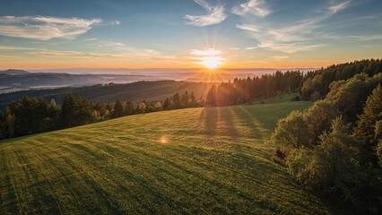 A scenic landscape of rolling green hills and dense forest under a setting sun with colorful sky and clouds, capturing a peaceful and natural environment at sunset.