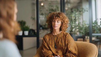 A thoughtful woman sits on a comfortable chair, engaging in a counseling session in a stylish, plant filled workspace. The scene highlights empathy, communication, and emotional well being