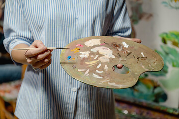 Artist holding a paint palette and brush, preparing to create artwork. Close-up of colorful oil paints on palette, creative studio atmosphere.
