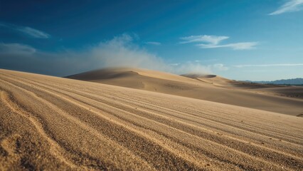 Obraz premium A vast desert landscape with sand dunes under a blue sky with clouds.