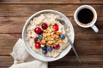 Oatmeal porridge with berries and cup of coffee on wooden table background, top view