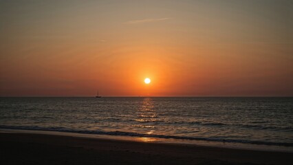 Fototapeta premium Sunset over the ocean from the beach, with the sun near the horizon and calm waters, creating a peaceful and scenic view.