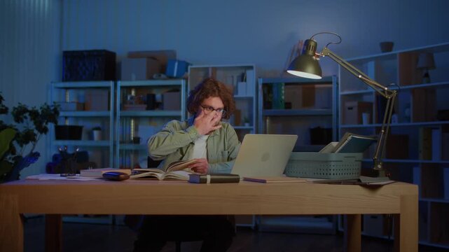 Exam Preparation. A young male student studies late at night surrounded by books and a laptop, symbolizing hard work, focus, and dedication in education under academic pressure.