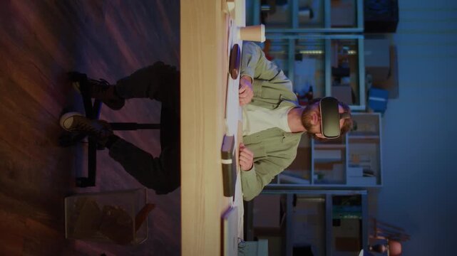 Vertical Video Bearded Man Wearing Virtual Reality Headset While Sitting At Desk With Laptop And Papers. Concept of Digital Innovation, Future Technology, VR Simulation, Remote Work