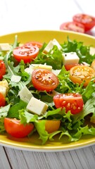 A bright yellow plate holds a colorful salad of greens, tomatoes, and chunks of cheese