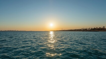 Fototapeta premium A sunset over the water with the horizon, showing a calm sea and a distant shoreline with palm trees. Idyllic scene at dusk or dawn.