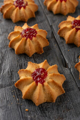 Close-Up of Six Flower-Shaped Cookies with Red Jam Centers on Rustic Wooden Surface