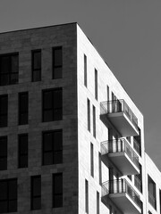 Striking black and white photo of the corner of a modern residential building. The textured facade, sharp geometric lines, and stacked balconies create an abstract, minimalist architectural design.