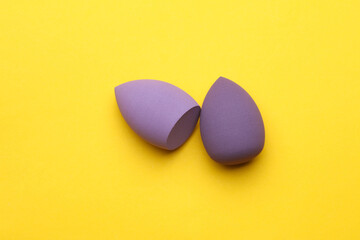 Fototapeta premium Makeup eggs shape blenders of purple color on yellow background. Beauty concept. Top view