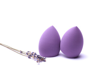 Makeup egg blenders of purple color with dry lavender on white background. Beauty concept.