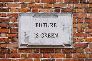 Fototapeta premium A stone plaque with the words FUTURE IS GREEN is mounted on a red brick wall. The message is promoting environmental consciousness and sustainable living