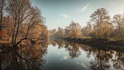 Obraz premium Autumn scene with trees along a calm river reflecting the sky and foliage. Nature landscape with water and seasonal trees in fall.