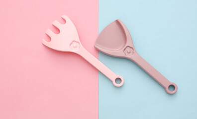 Children's plastic shovel and rake for sandbox on blue pink background
