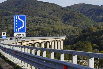 A suspension bridge in a mountainous landscape.The bridge, with its concrete supports, curves through the green mountain landscape. The picturesque road winds through hills and forests on a sunny day.