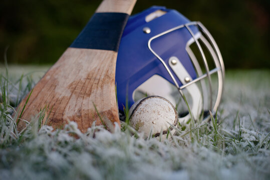 Gaelic Irish origin hurley, helmet, and ball lie on frosty grass in outdoor field, suggesting cold morning practice, hurling sport gear ready for play. National Irish game hurling