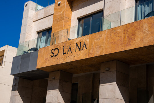Close view of Solana Hotel and Spa entrance in Mellieha, Malta, with ochre stone overhang, glass balconies, SOLANA signage, and modern rooms under bright daylight.