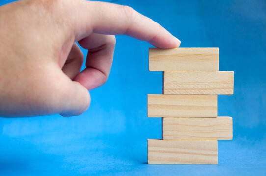 Hand holding wooden block above stacked pieces on blue background showing building and growth concept with customizable space for text or ideas.