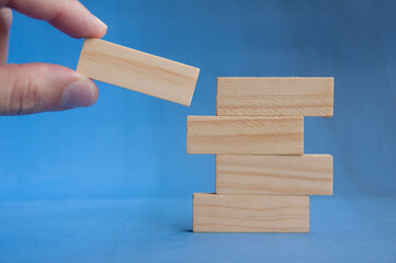 Hand preparing to place wooden block on lower stack showing teamwork and foundation concept with customizable space for text or ideas.
