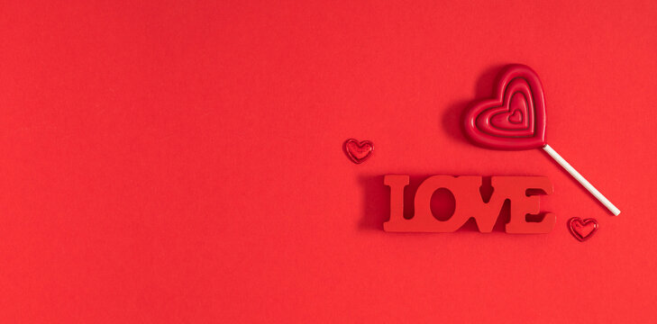 Valentine’s Day minimal composition with red heart-shaped lollipop, LOVE text, and small hearts on red background. Romantic flat lay with copy space for love, holiday, and relationship concept
