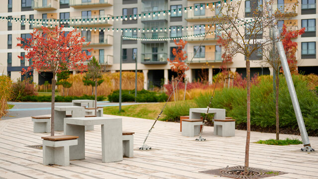 modern urban courtyard scene features concrete benches and autumn trees near apartment buildings. inviting outdoor space ideal for relaxation and community gatherings, with string lights creating