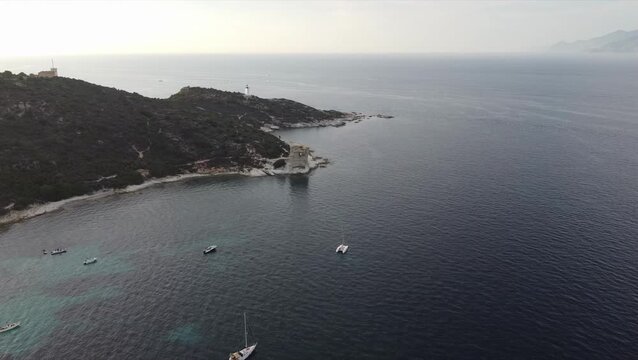 Aerial view Tour de la Mortella Tower and lighthouse, Cap Corse, Corsica, France. Historic Genoese coastal watchtower surrounded by clear Mediterranean waters.
