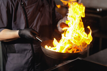 Male chef France flambe cooking in commercial kitchen with frying pan