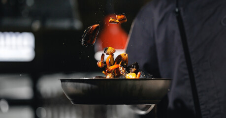Chef in dark apron flipping sauteed vegetables in frying pan