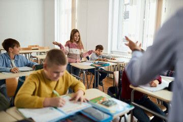 Uncertain elementary student talking  with her teacher during a class in the classroom.