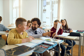 Happy male teacher talking with his elementary student while teaching him on a class in the classroom