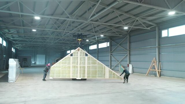 Valka, Latvia - October 29, 2025: Workers maneuvering a large wooden structure in a spacious warehouse, camera follows with a smooth dolly motion
