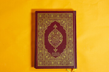 A closed copy of the Holy Quran with Arabic calligraphy on a green cover. The Arabic text reads “Al-Qur’an Al-Kareem,” which means “The Holy Quran.” Image for educational and cultural purposes
