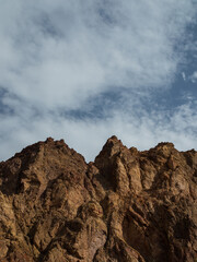 Cliffs against the sky, an old brown mountain peak, bare and rocky, against a blue sky with small clouds, the top