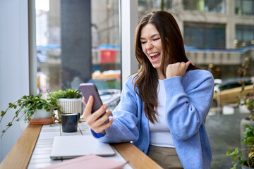 Happy young woman student feeling excited winner holding cellphone using mobile phone winning...