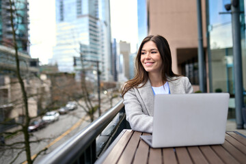 Young happy business woman worker or student working on laptop computer outdoors in outdoor cafe....