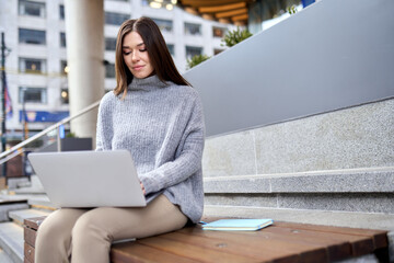 Young happy business woman worker or student working on laptop computer outdoors in campus area....