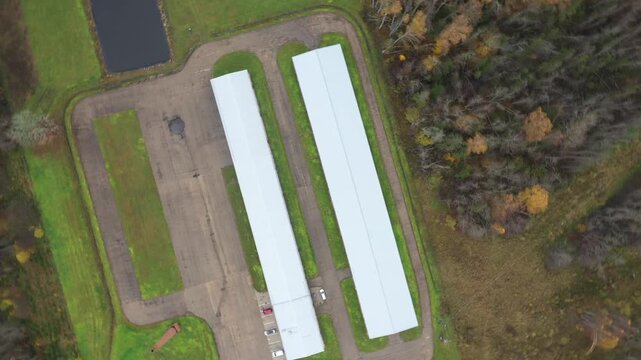Valka, Latvia - October 29, 2025: Aerial view of agricultural storage buildings with surrounding greenery, camera pans to reveal expansive landscape